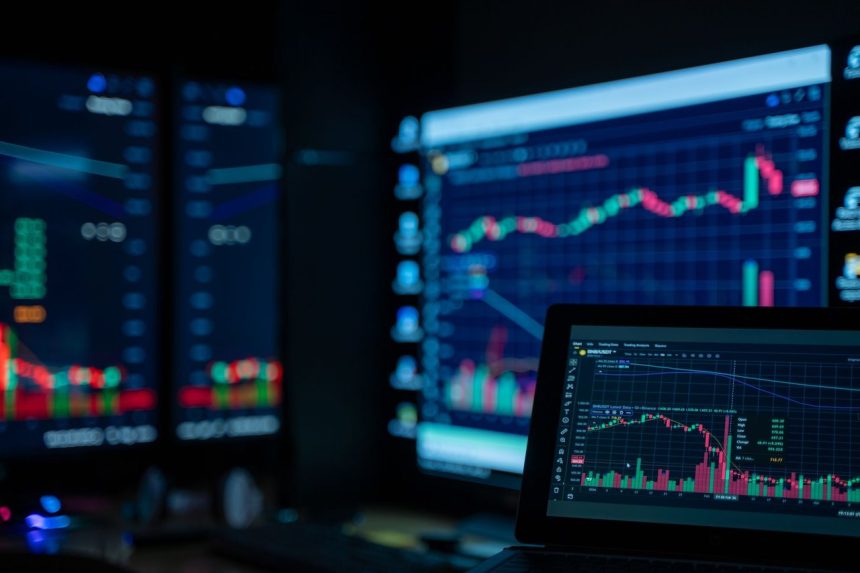 Monitores exibem gráficos e dados do mercado financeiro em uma sala de operações.