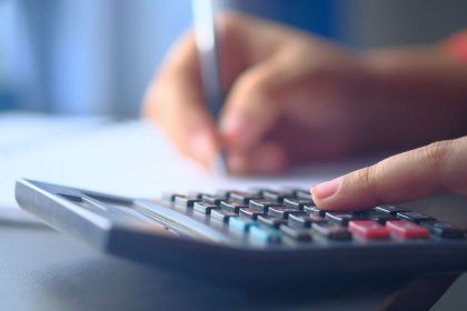 Mãos usando uma calculadora e fazendo anotações para organizar o orçamento doméstico.