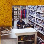 Homem trabalha em uma pequena sala de armazenamento repleta de ferramentas e equipamentos.