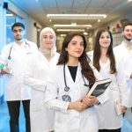 Grupo de estudantes de medicina usando jalecos conversa em um corredor de universidade.