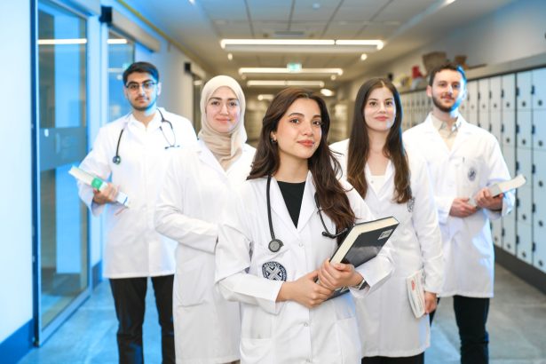 Grupo de estudantes de medicina usando jalecos conversa em um corredor de universidade.